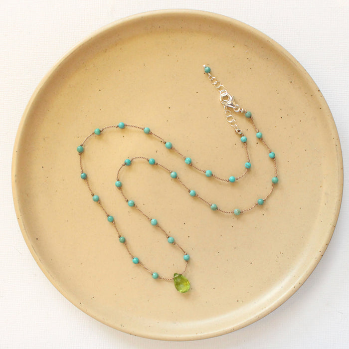 The knotted turquoise and peridot drop necklace styled on a tan plate to show the adjustable lobster clasp closure