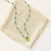 The knotted turquoise and peridot drop necklace styled on tan linen