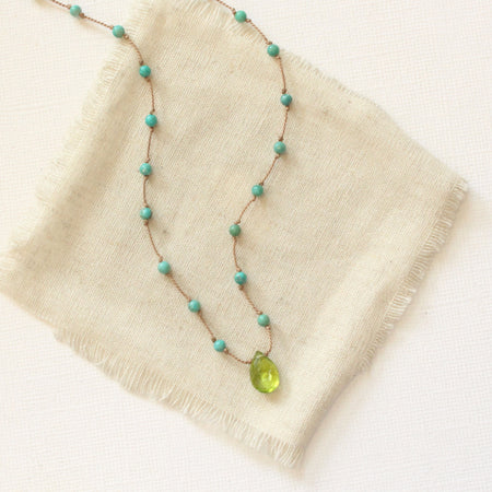 The knotted turquoise and peridot drop necklace styled on tan linen