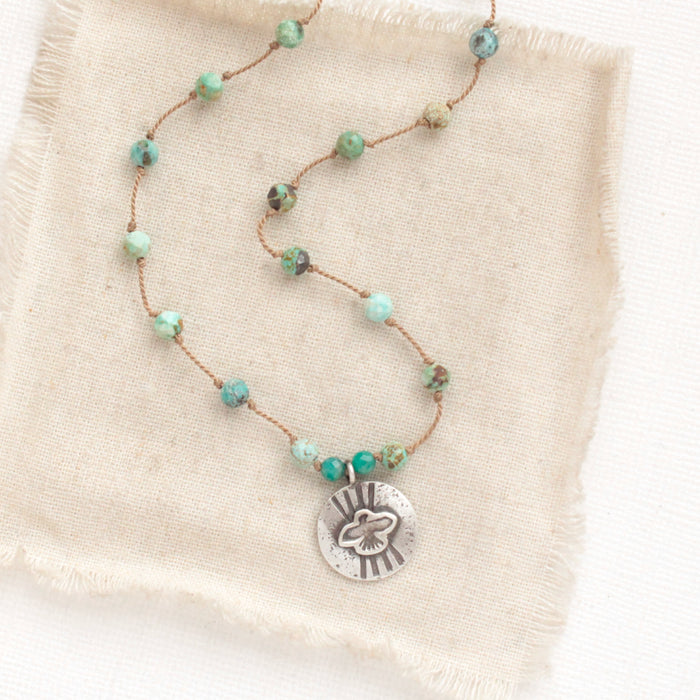 The knotted turquoise soar necklace styled on tan linen