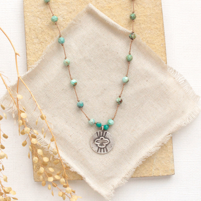 The knotted turquoise soar necklace styled on a tan rock with linen and dried grass
