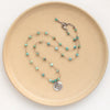 The knotted turquoise soar necklace styled on a tan plate to show the adjustable lobster clasp closure