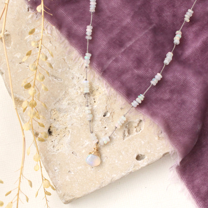 The knotted opal necklace styled on a tan rock with purple velvet and dried grass