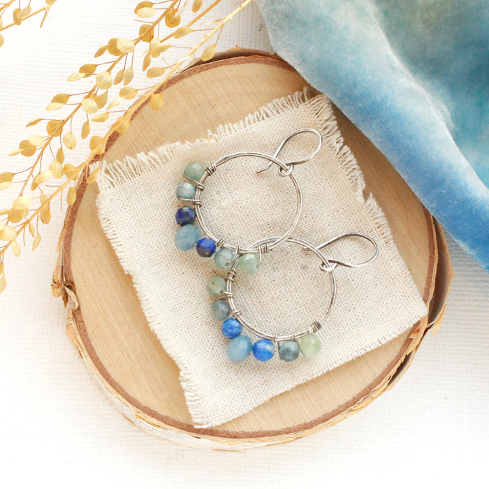 The kyanite and aquamarine hoop earrings styled on wood with blue velvet and dried grass