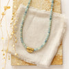 The beaded kyanite mythos necklace styled on a tan rock with linen and dried grass