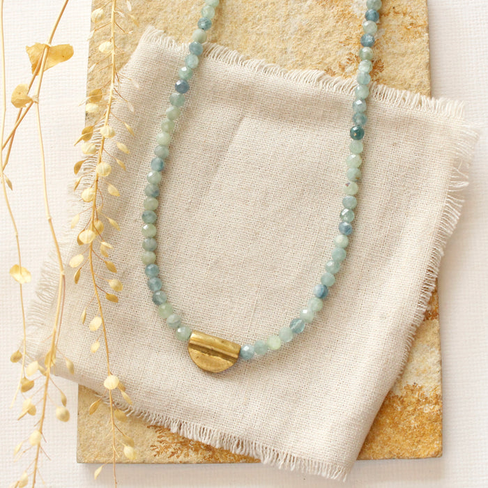 The beaded kyanite mythos necklace styled on a tan rock with linen and dried grass
