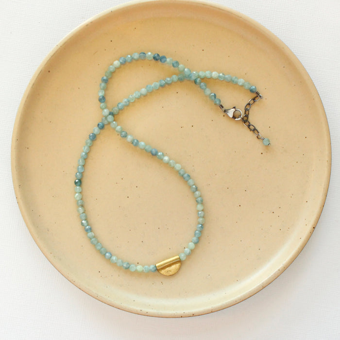 The beaded kyanite mythos necklace styled on a tan plate to show the adjustable lobster clasp closure