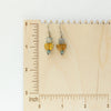 The stacked mythos earrings styled on a wooden ruler for size reference