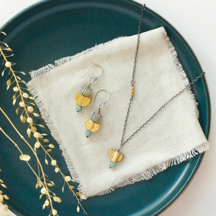 The stacked mythos earrings styled on a blue plate with the matching necklace
