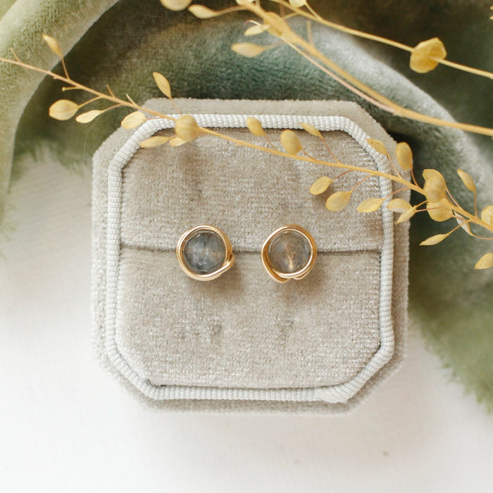 The gold wrapped labradorite post earrings styled on a velvet box with green velvet and dried grass