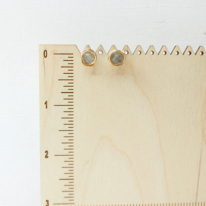 The gold wrapped labradorite post earrings styled on a wooden ruler for size reference