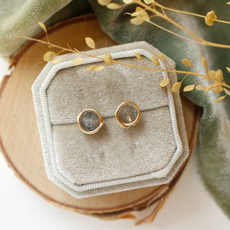 The gold wrapped labradorite post earrings styled on wood with green velvet and dried grass