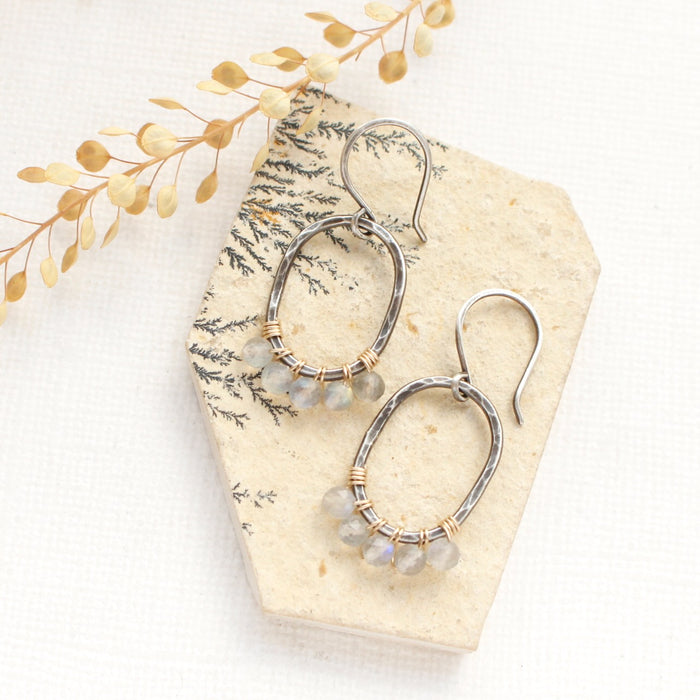 The labradorite wrapped mixed metal hoop earrings styled on a tan rock with dried grass