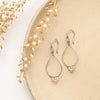 The labradorite wrapped teardrop hoop earrings styled on a tan plate with dried grass
