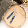 The lapis beaded bar earrings styled on wood with gray velvet and dried grass