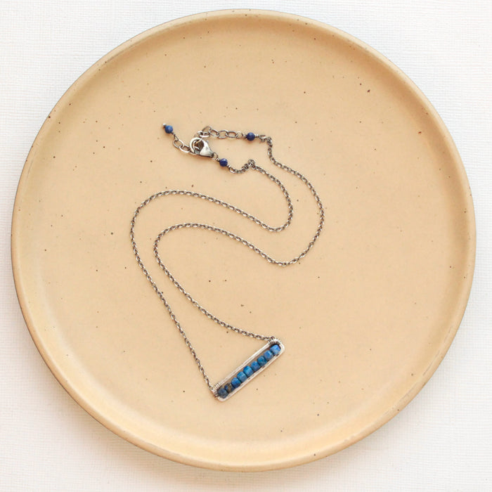 The lapis beaded bar necklace styled on a tan plate to show the adjustable lobster clasp closure