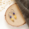 The lapis and brass leaf earrings styled on wood with gray velvet and dried grass