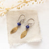 The lapis and brass leaf earrings styled on tan linen with dried grass