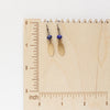 The lapis and brass leaf earrings on a wooden ruler for size reference