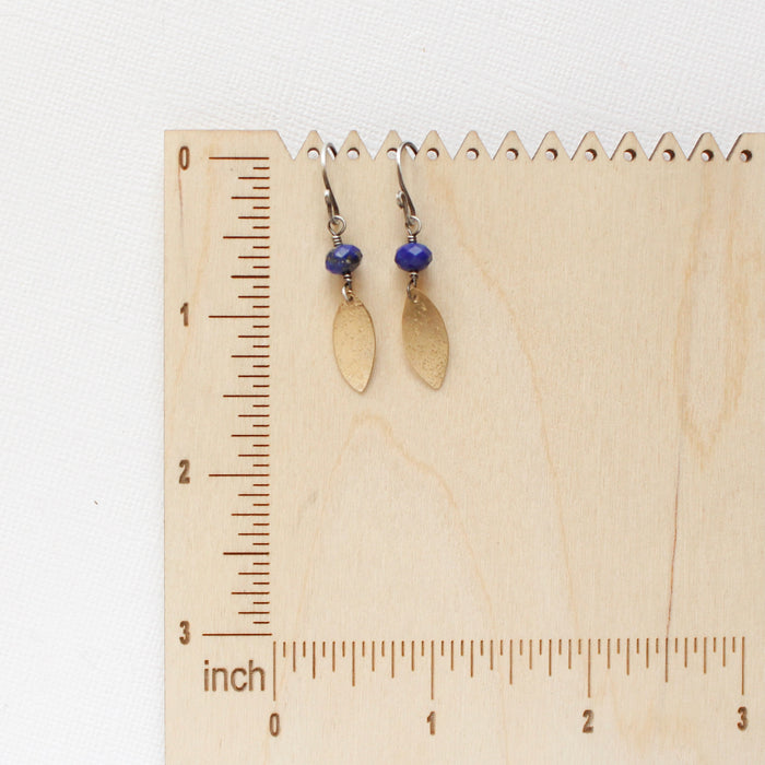 The lapis and brass leaf earrings on a wooden ruler for size reference