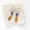 The lapis and brass leaf earrings styled on tan linen