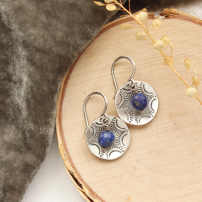 The lapis cupped jolie earrings styled on wood with gray velvet and dried grass