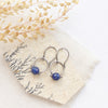 The lapis la cloche earrings styled on a tan rock with linen and dried grass