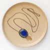 The lapis and brass leaf long necklace styled on a tan plate to show the whole silver cable chain