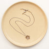The bronze layered cactus flower necklace styled on a tan plate to show the adjustable lobster clasp closure