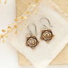 The bronze layered cactus flower earrings styled on a tan rock with linen and dried grass