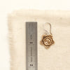 A bronze layered cactus flower earring next to a ruler for size reference