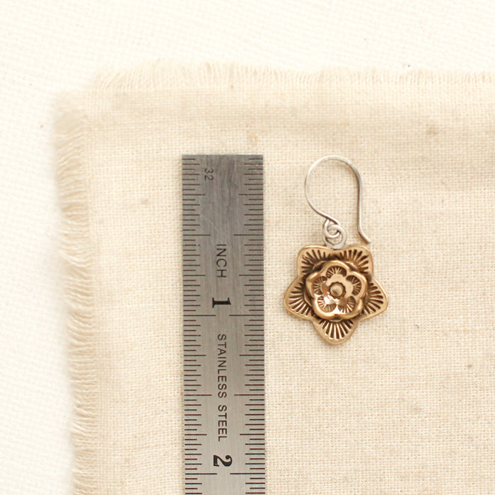 A bronze layered cactus flower earring next to a ruler for size reference