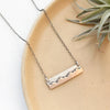 The oxidized silver layered mixed metal mountain bar necklace styled on a tan plate with an air plate