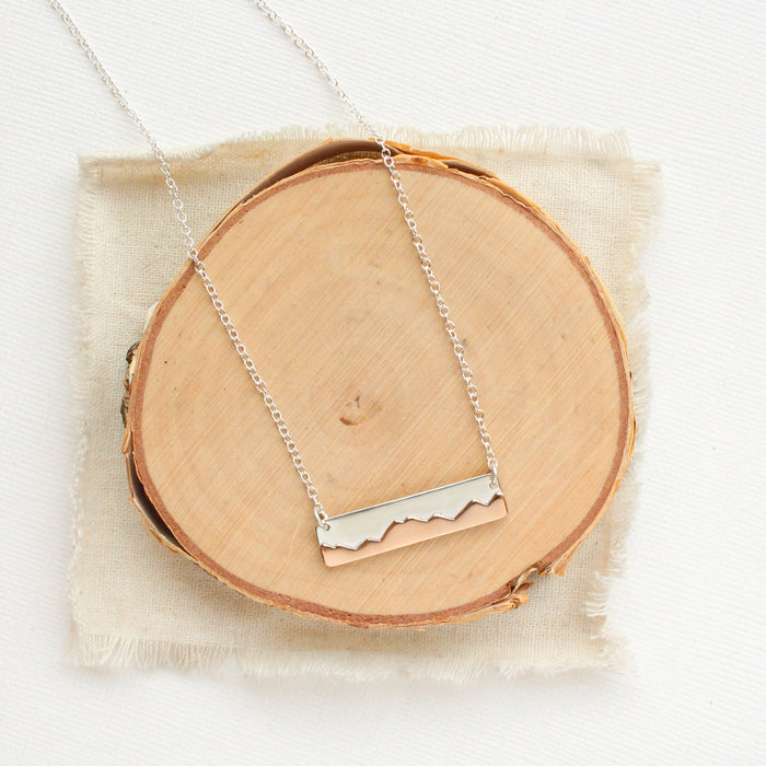 The bright silver layered mountain bar necklace styled on wood with linen