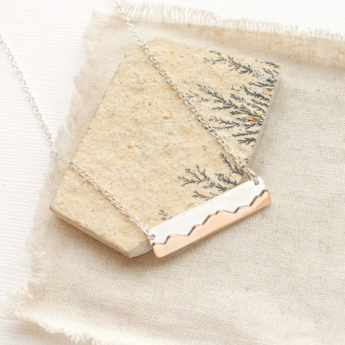 The bright silver layered mountain bar necklace styled on a tan rock with linen