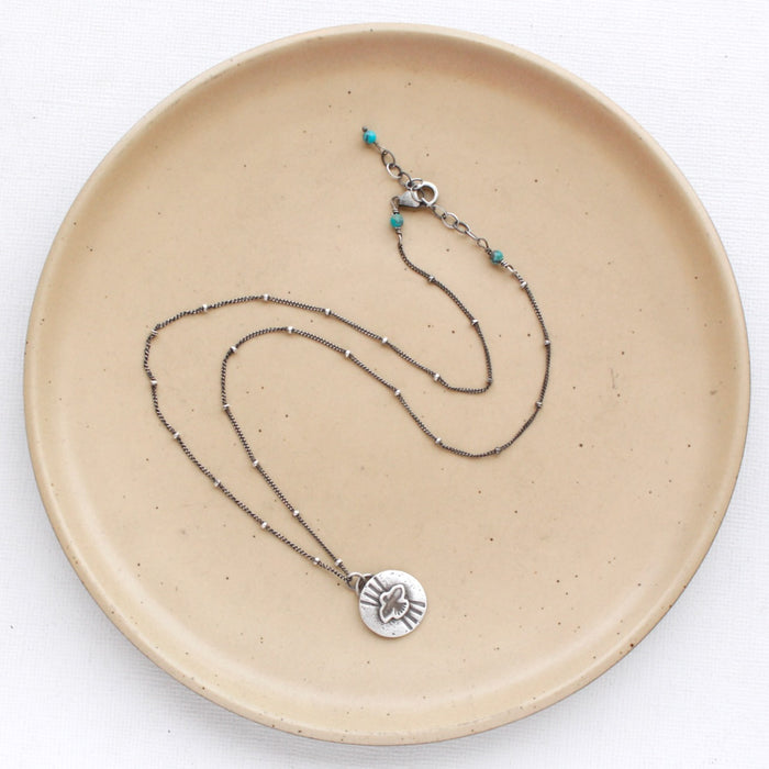 The layered soar necklace styled on a tan plate to show the adjustable lobster clasp closure