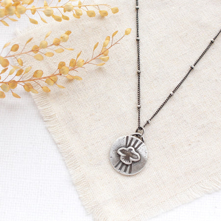 The layered soar necklace styled on tan linen with dried grass