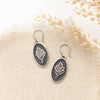 The layered sprout earrings styled on tan linen with dried grass
