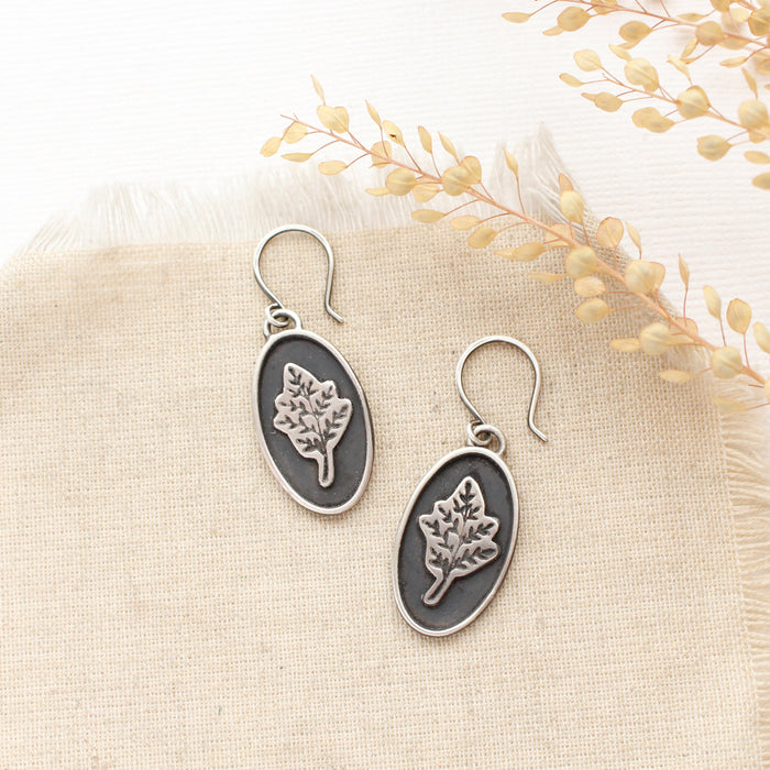 The layered sprout earrings styled on tan linen with dried grass