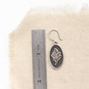 A layered sprout earring next to a ruler for size reference