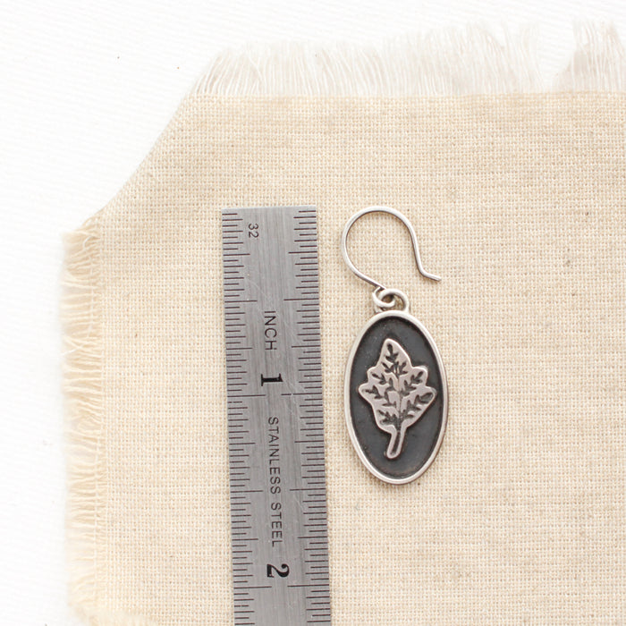 A layered sprout earring next to a ruler for size reference