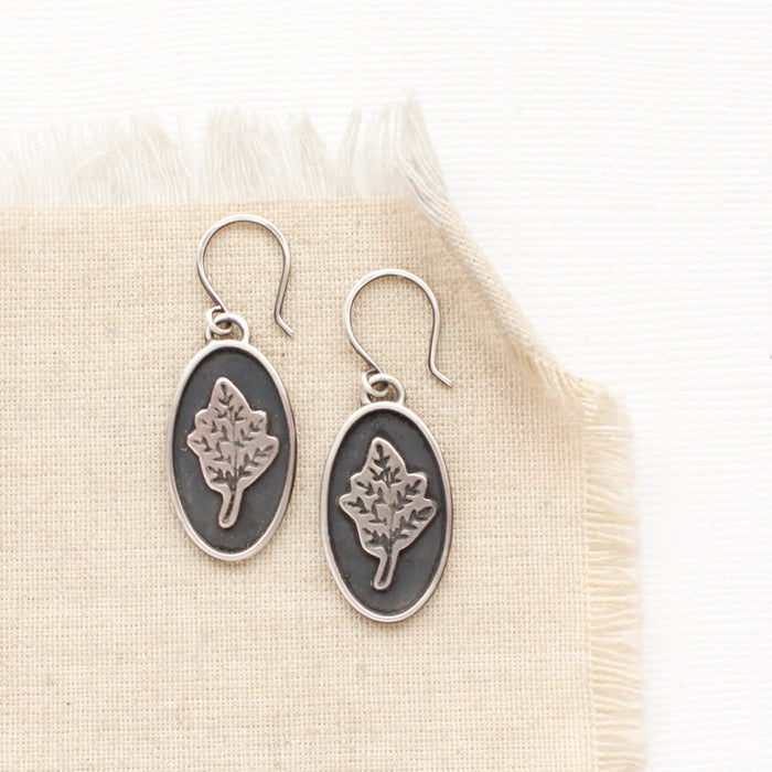 The layered sprout earrings styled on tan linen