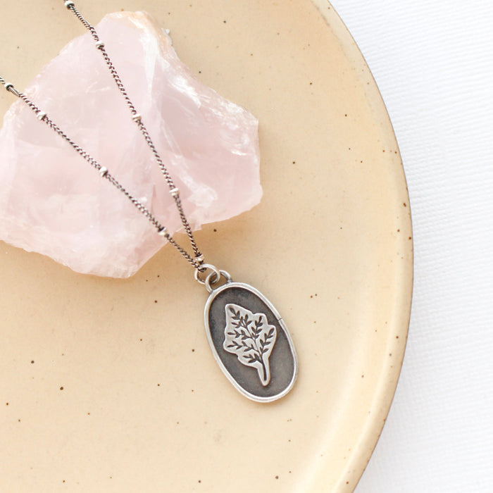The layered sprout necklace styled on a tan plate with a pink stone
