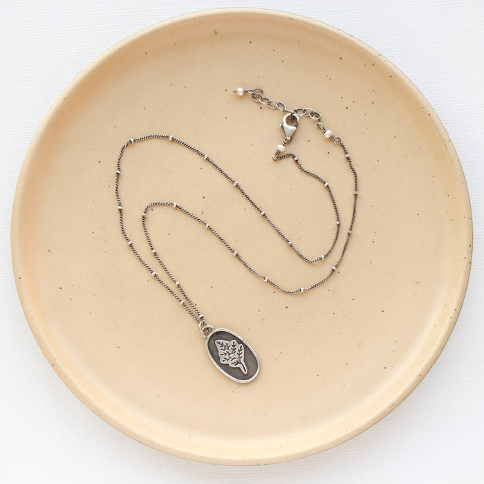 The layered sprout necklace styled on a tan plate to show the adjustable lobster clasp closure