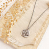The layered wanderer coin necklace styled on a ran rock with linen and dried grass