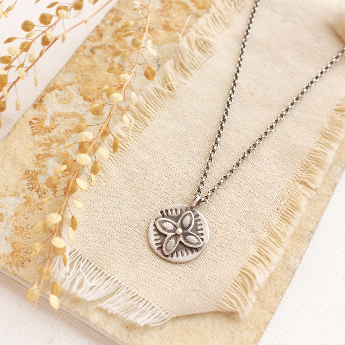 The layered wanderer coin necklace styled on a ran rock with linen and dried grass