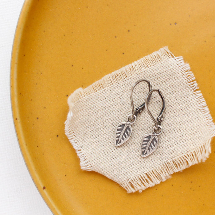 The leaf charm earrings styled on a yellow plate with tan linen