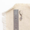 A leaf charm earring next to a ruler for size reference