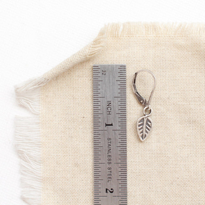 A leaf charm earring next to a ruler for size reference