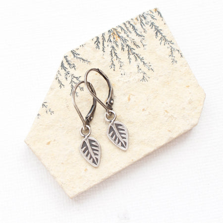 The leaf charm earrings styled on a tan rock